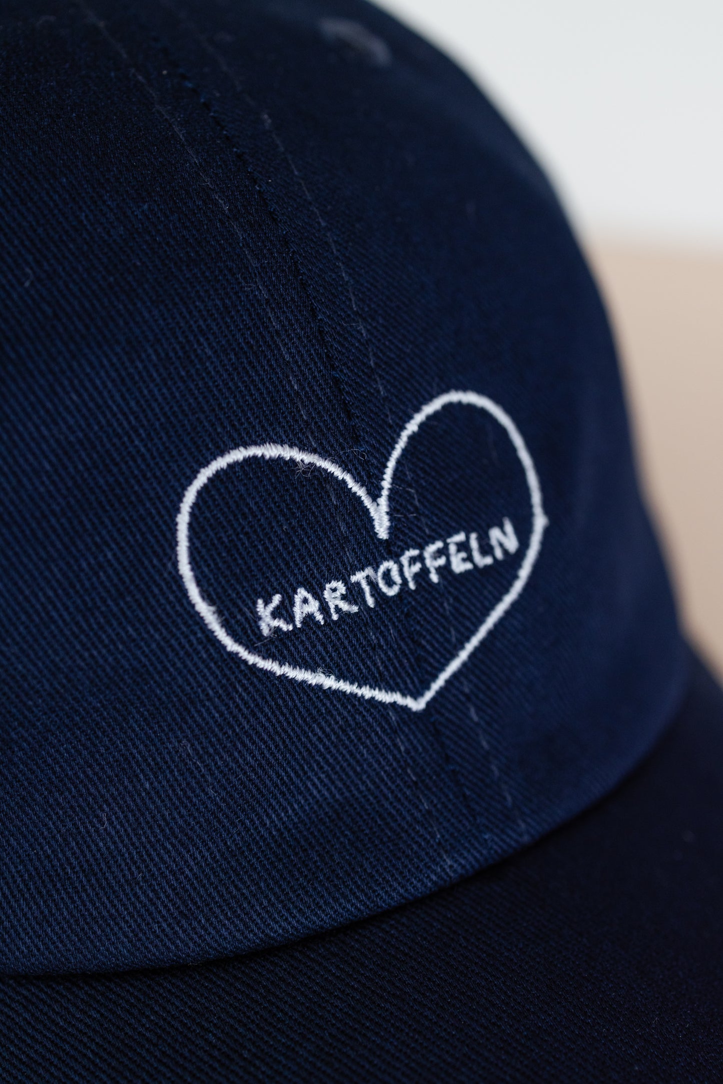Detail Ansicht einer dunkelblauen Kappe mit weißer Stickerei ‚Kartoffeln‘ in Herzform