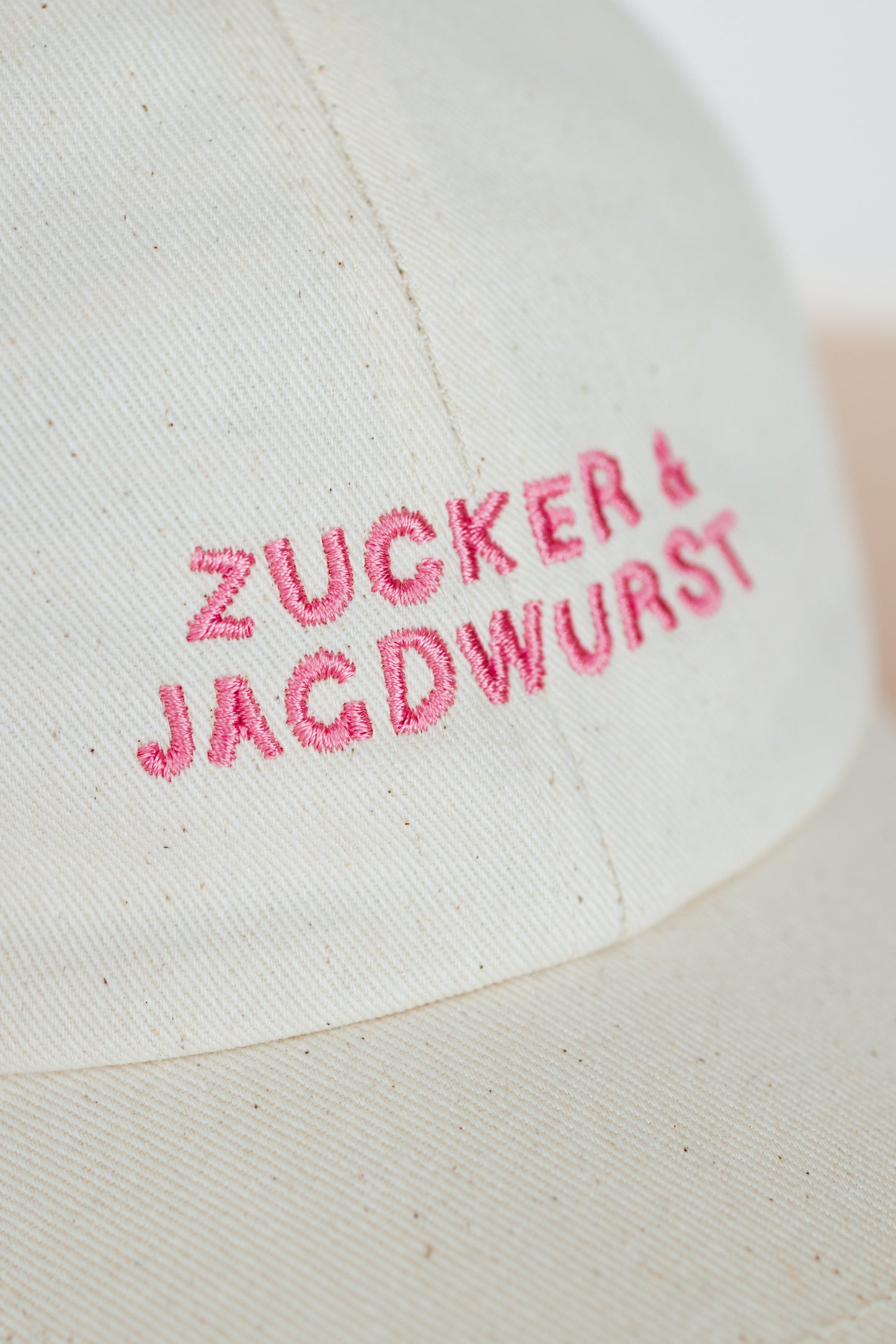 Detailaufnahme einer weißen Kappe mit pinker Stickerei ‚Zucker & Jagdwurst‘
