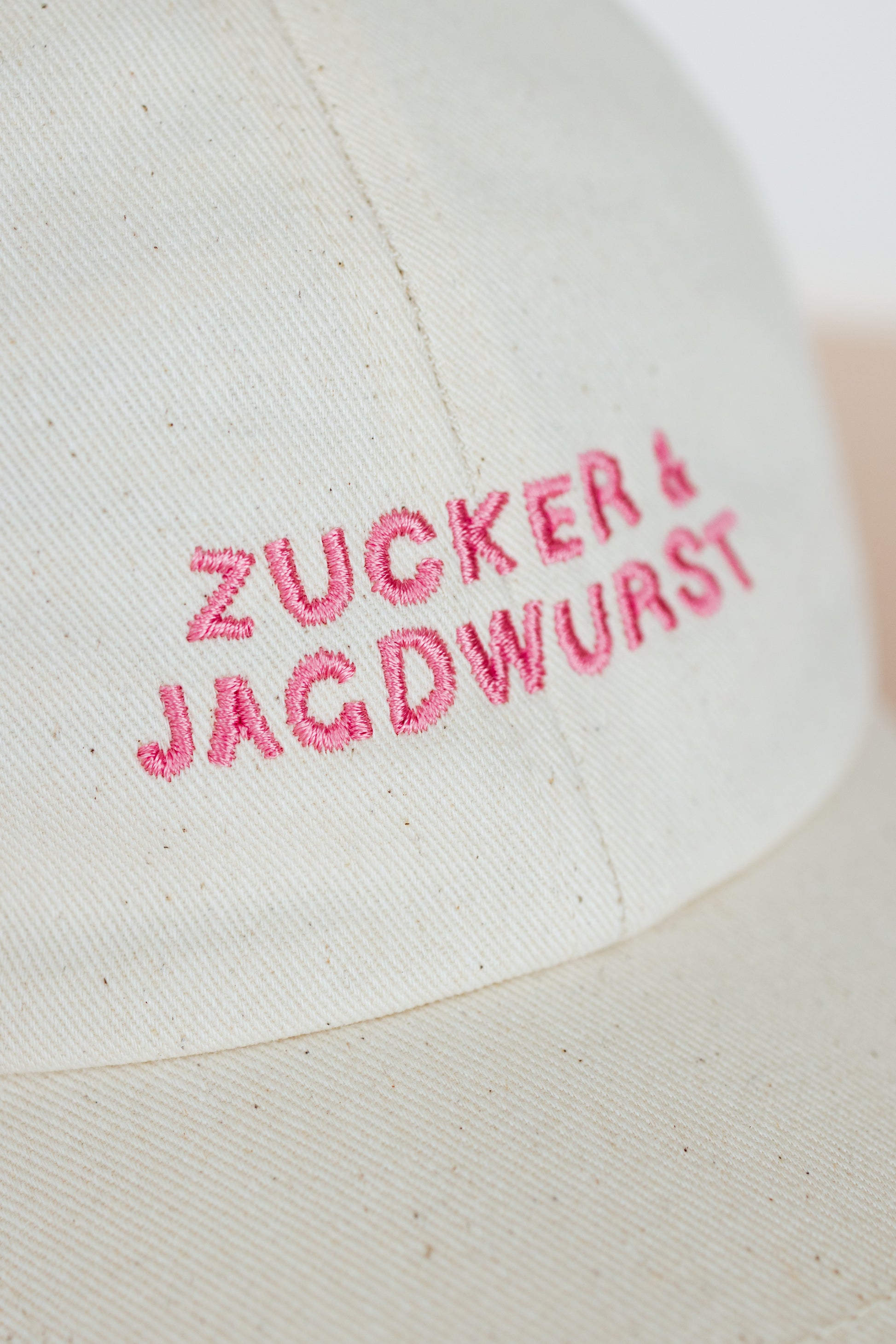 Detailaufnahme einer weißen Kappe mit pinker Stickerei ‚Zucker & Jagdwurst‘