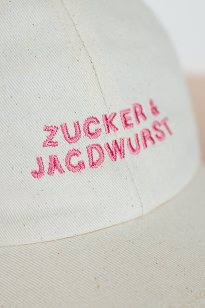Detailaufnahme einer weißen Kappe mit pinker Stickerei ‚Zucker & Jagdwurst‘